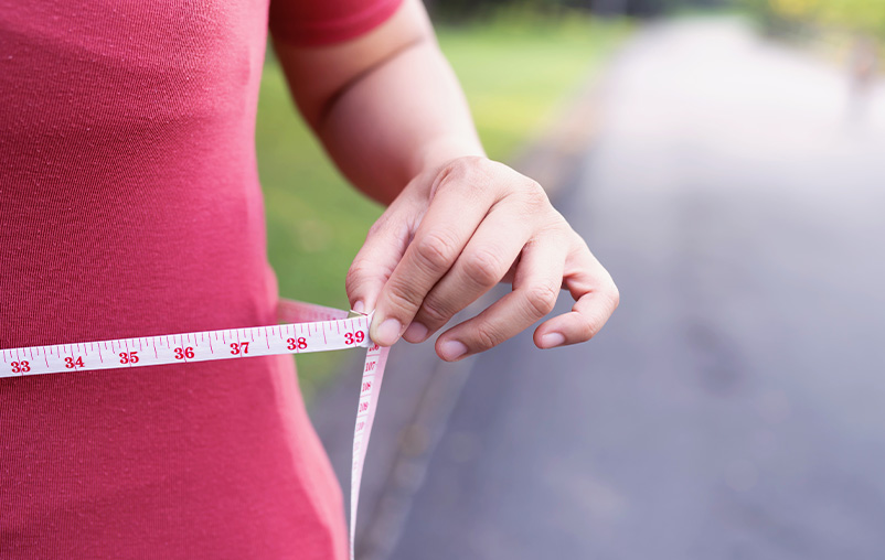 A woman holds a measuring tape loosely around her waist.