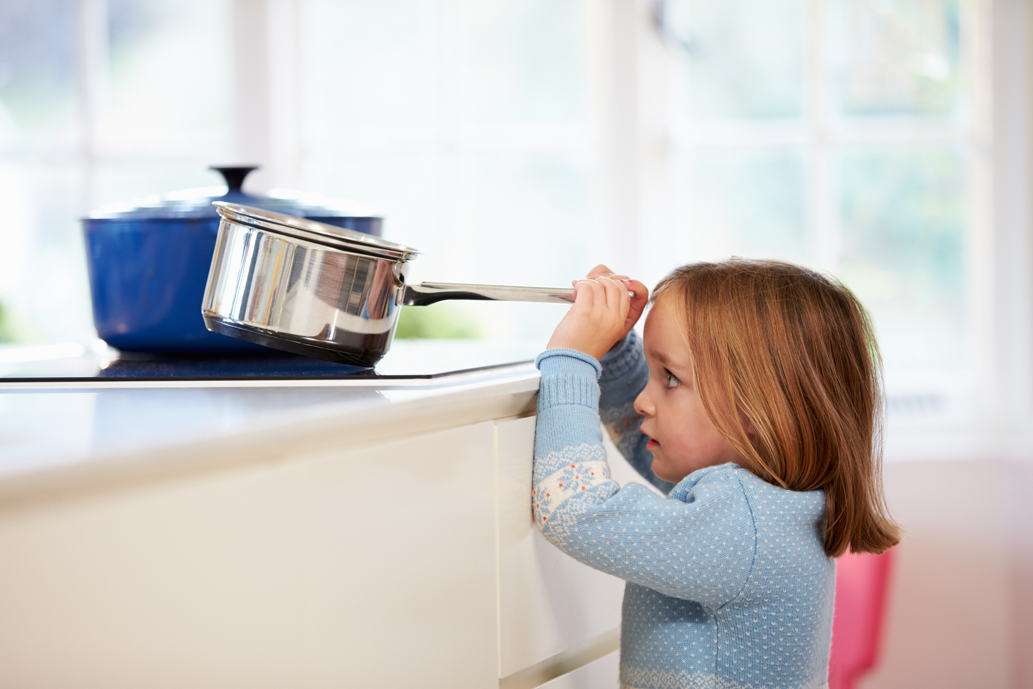 Small girl pulling a pan off the stove, risking injury