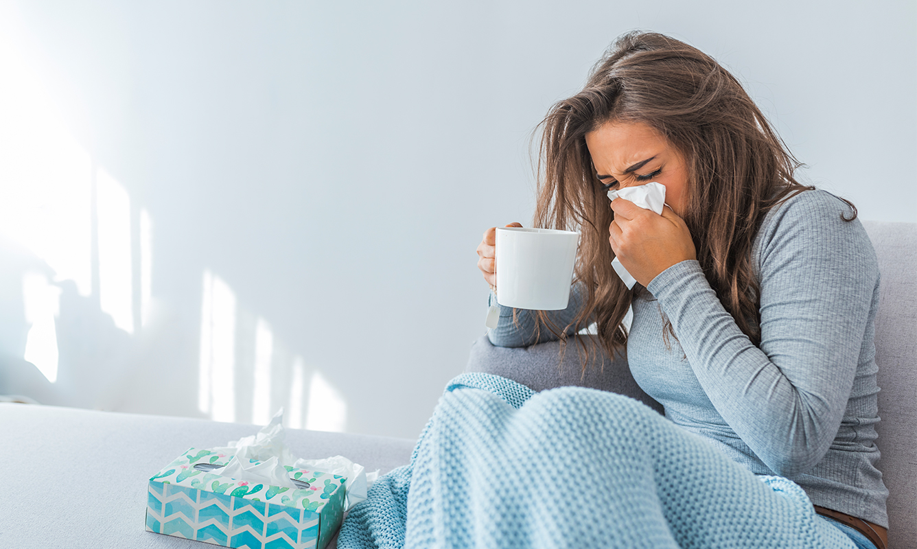 woman on couch with cup of tea and tissues fighting the flu