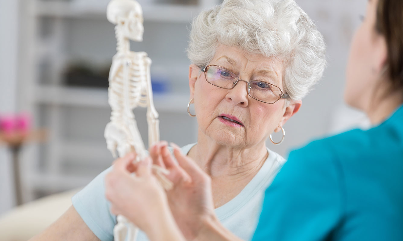Older women talking to someone about her bones. She is holding a miniature skeleton.