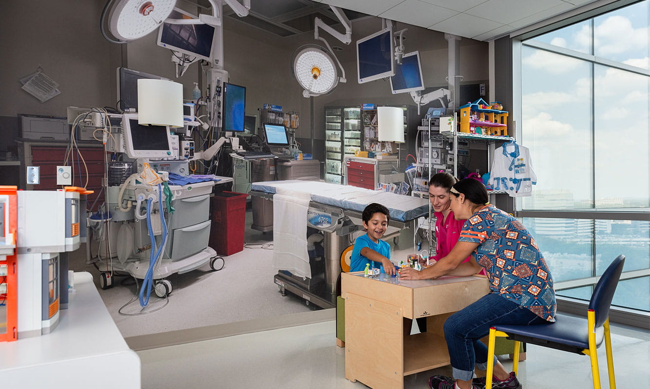 Child Life specialist does role play with mother and son at table in operating room before procedure