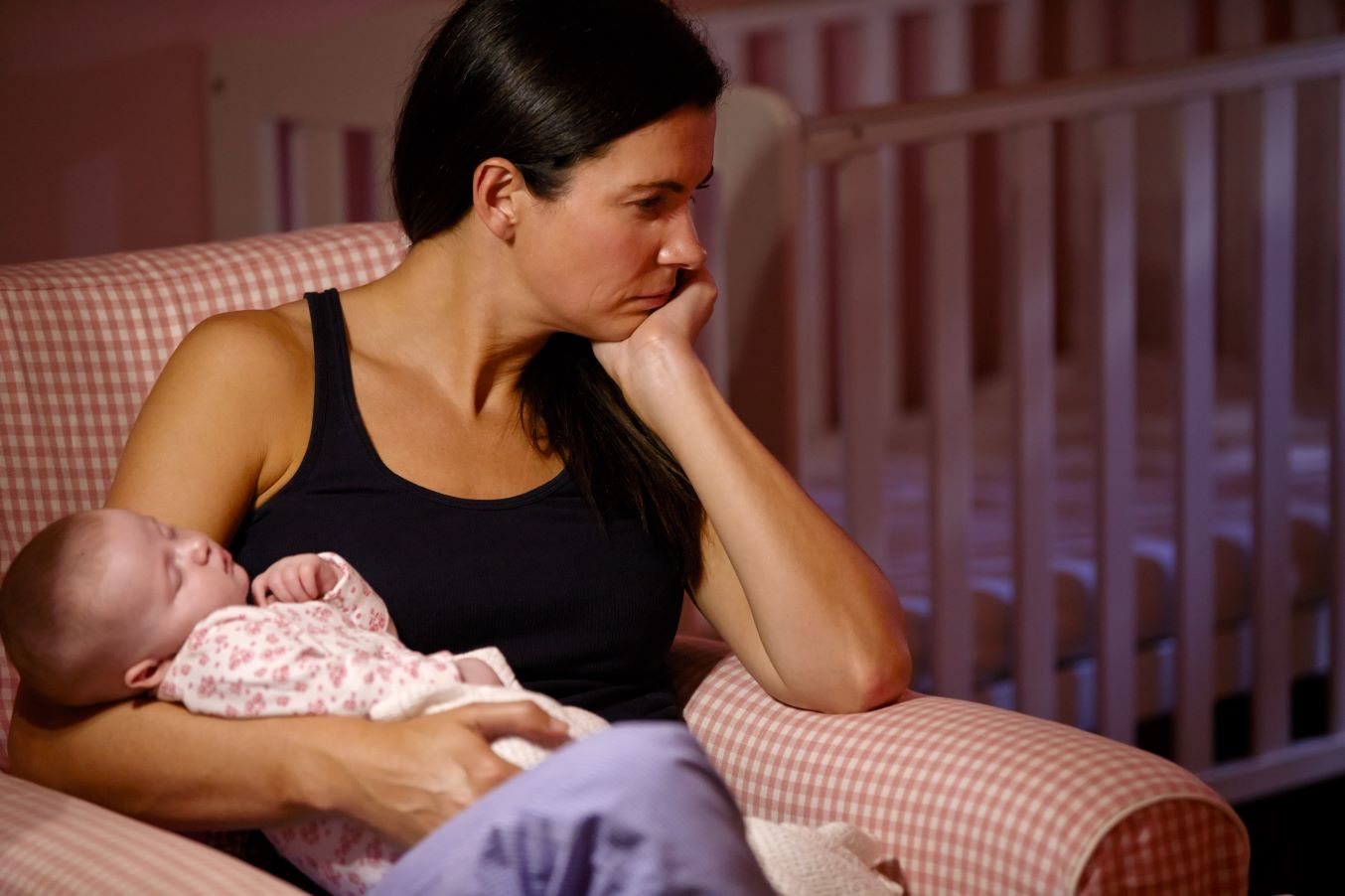 A woman cradles a baby but is frowning and looks distracted.