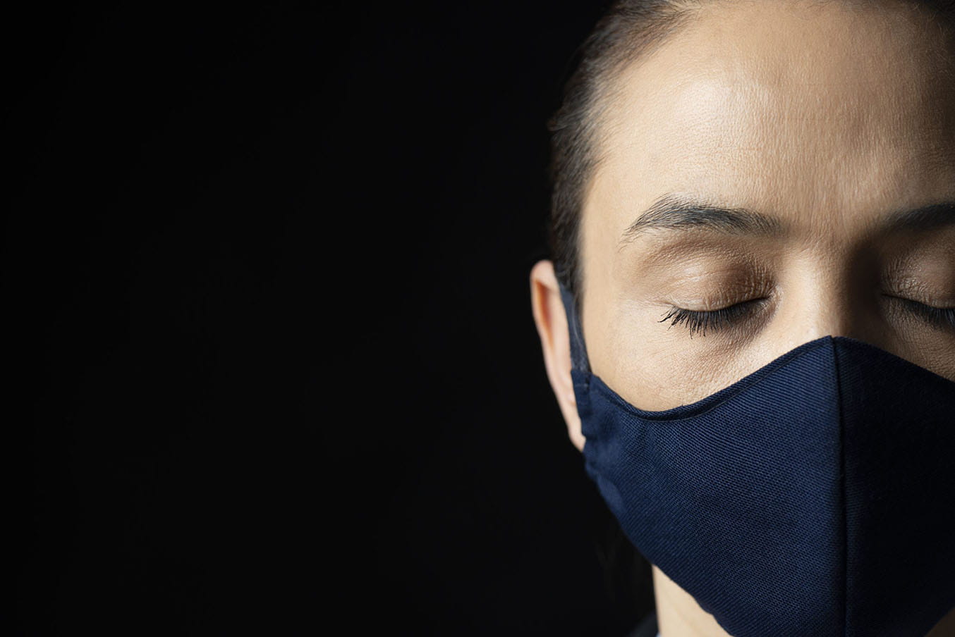 A woman wearing a mask has her eyes closed