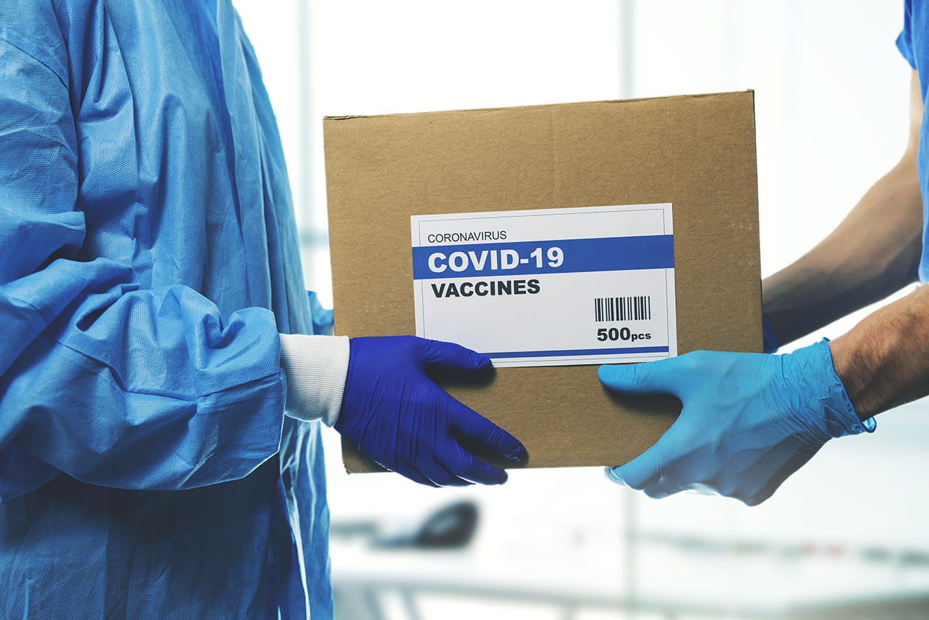 One person hands over a box labeled COVID-19 vaccines to another person