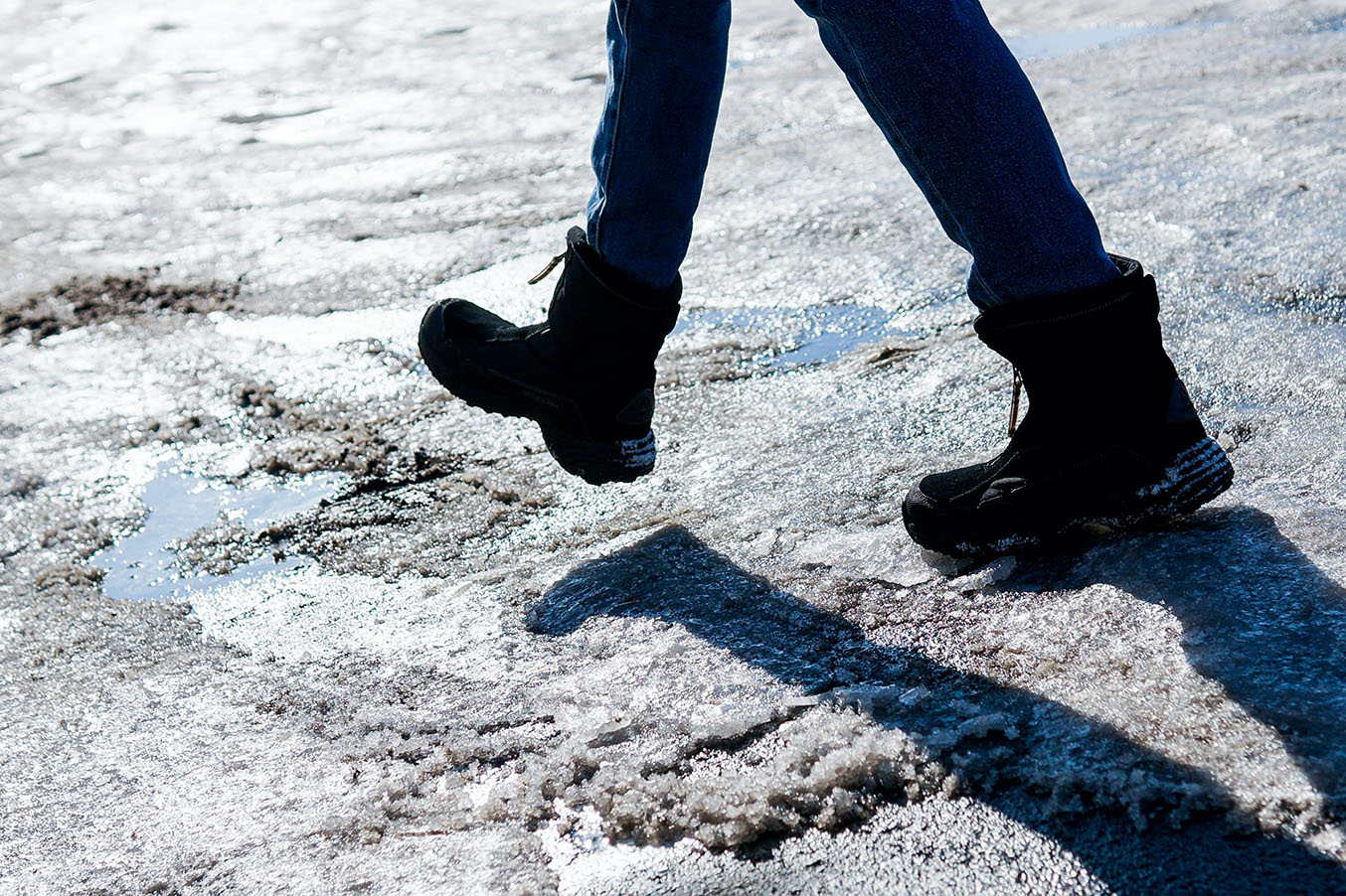 Someone walks on icy pavement wearing snow boots