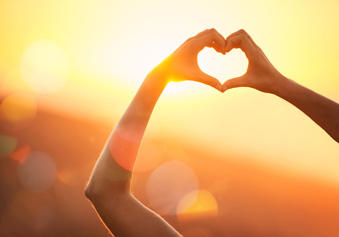 A woman holds up her hands to make a heart shape in the sun.