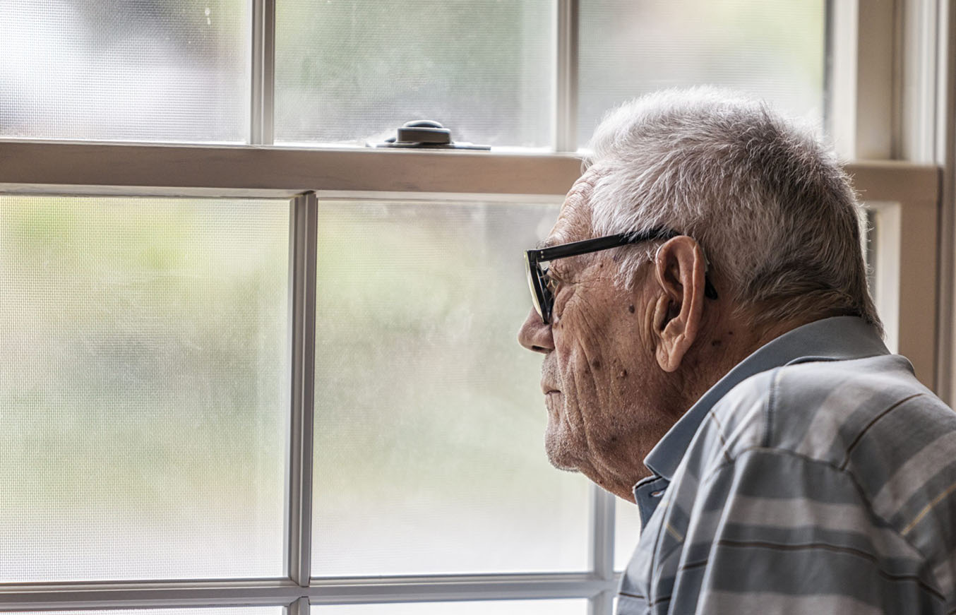 An elderly man looks out the window