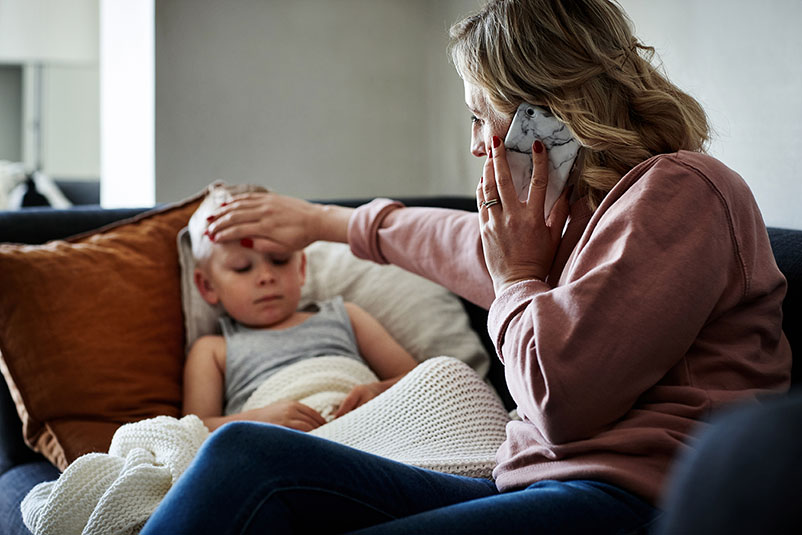 A mother holds her hand on a child's forehead while talking on the phone. 