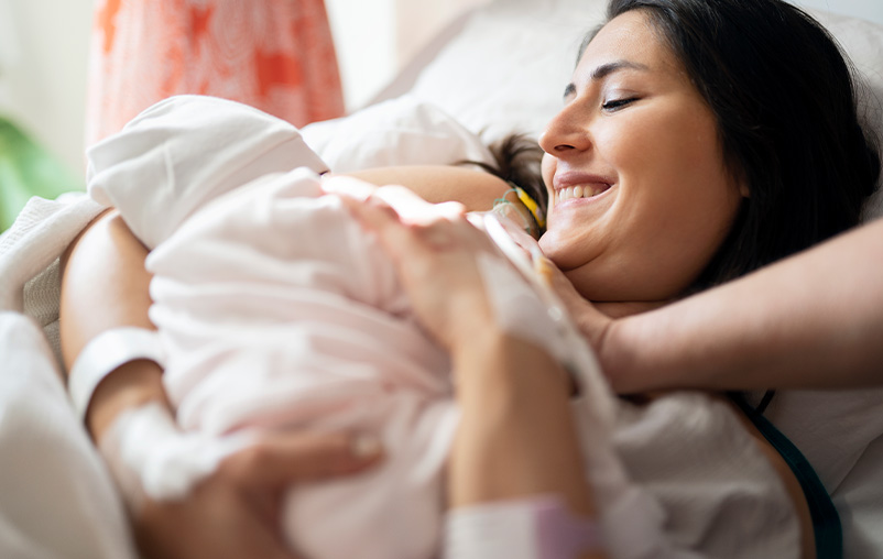 A woman smiles and holds her newborn.