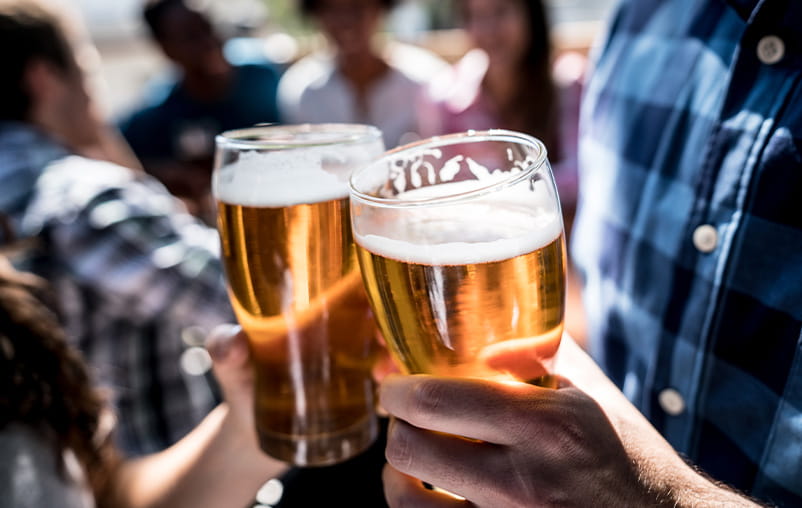 Two adults cheers with their pints of beer outdoors.