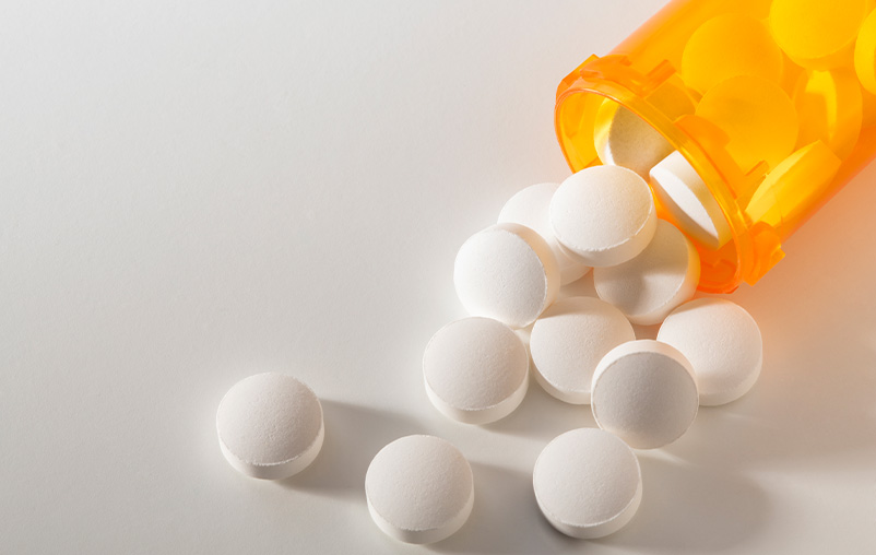 White pills spill out of an orange pill bottle.