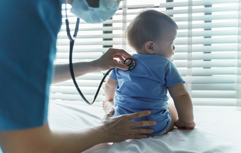 A medical provider holds a stethoscope to a baby's back.