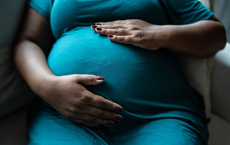 A pregnant Black woman with hands on her belly.