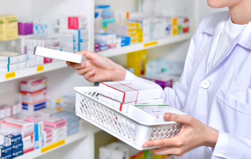 A pharmacist restocks a shelf of medications.