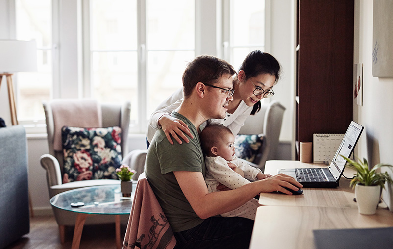 A man, woman and baby are gathered around a laptop.