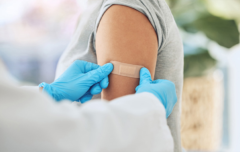 A health care worker puts a Band-Aid on a female patient's arm after administering a vaccine.