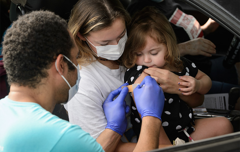University Health Pharmacy Programs Manager Ekenechukwu Ogogor places a Band-Aid on the arm of a young flu shot recipient during a drive-in flu vaccination clinic at the Joe and Harry Freeman Coliseum.