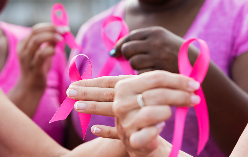 Closeup of women holding pink breast cancer awareness ribbons.