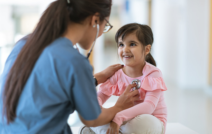 A health care worker uses a stethoscope to listen to a girl's heartbeat.