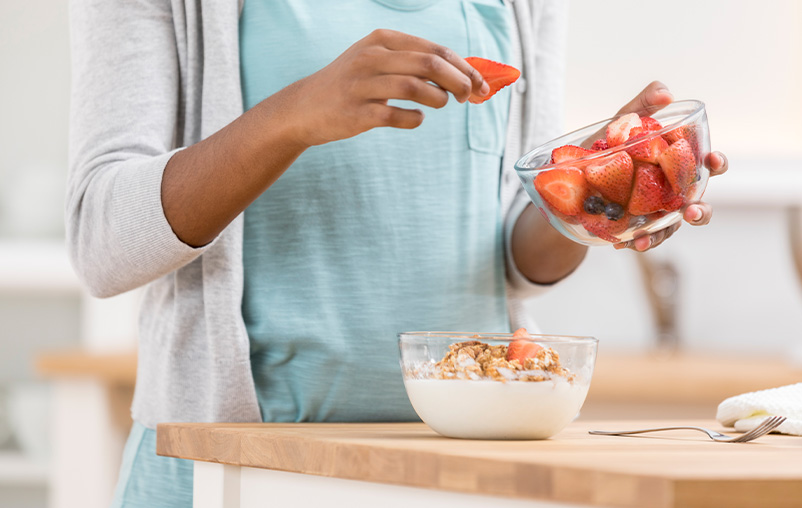 A woman puts fresh strawberries in a bowl of yogurt.