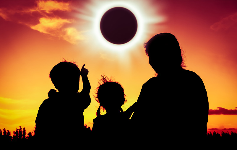 Two children and an adult watch a total solar eclipse.