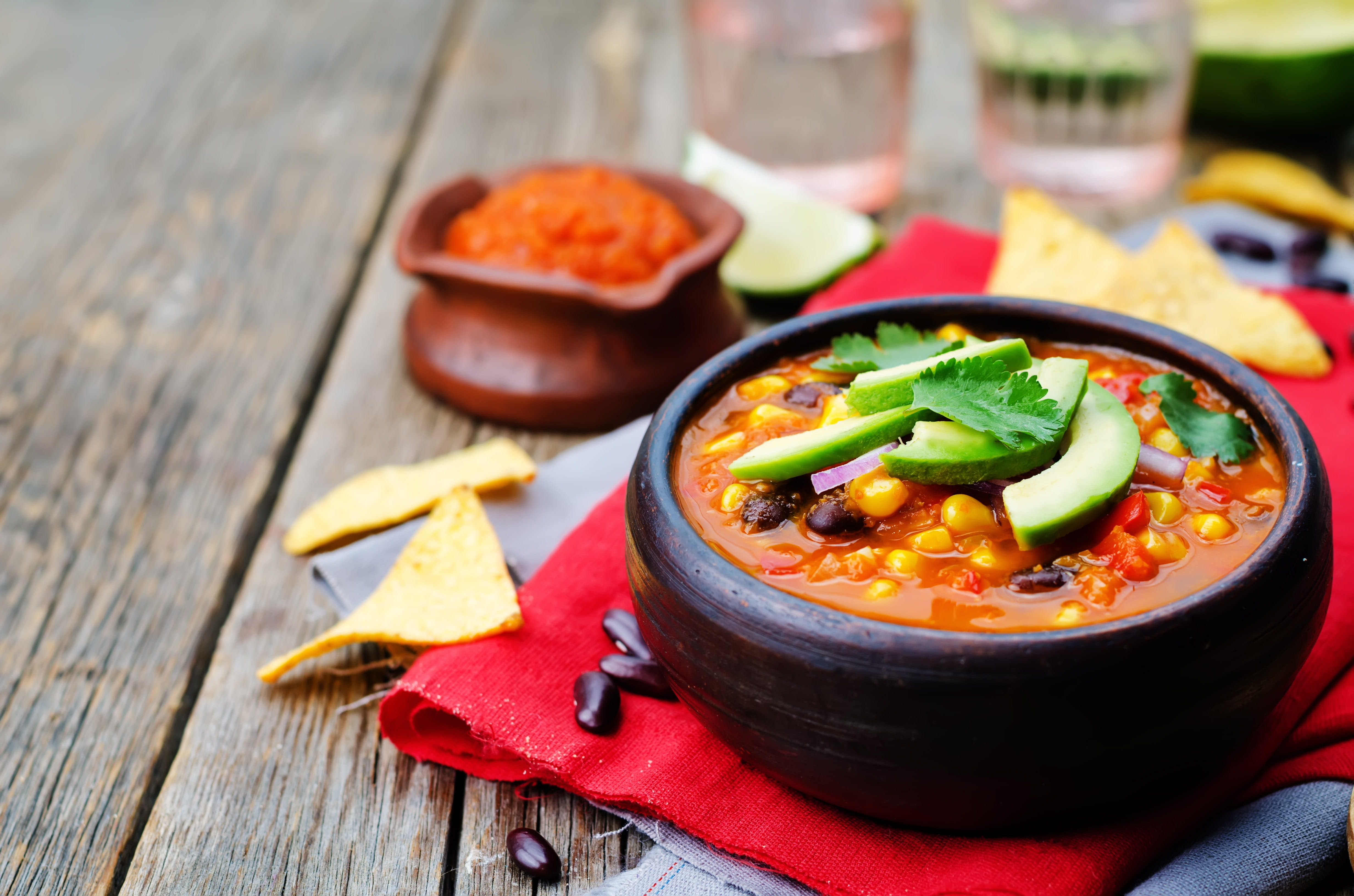 Vegan tortilla soup in a bark bowl with avocado slices on top.