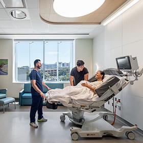 Pregnant woman in a child delivery room reenacting giving birth with a delivery nurse and her spouse present..