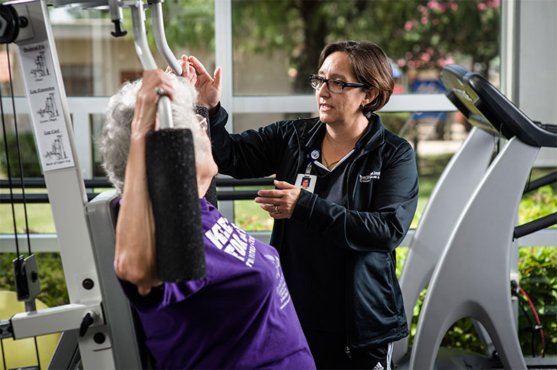 Medical specialist assisting woman exercising in fitness center gym