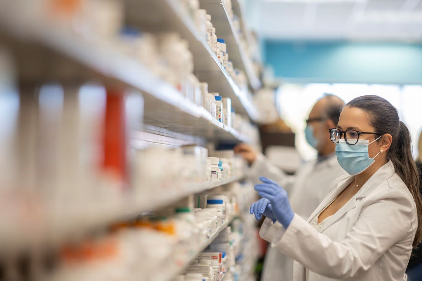 Pharmacist looking at shelves of medications behind the pharmacy counter.