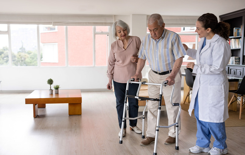 Man walks with a walker and with the assistance of a doctor and his wife