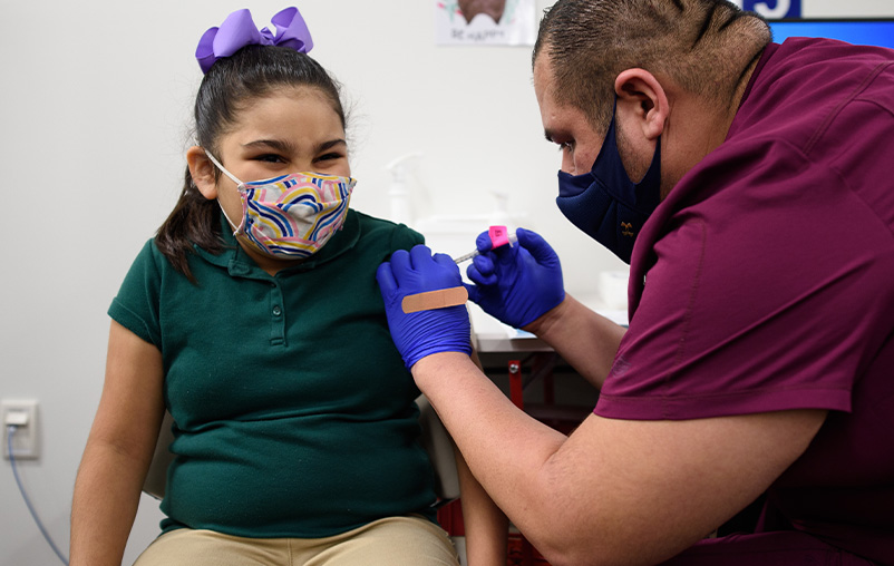 A little girl wearing a purple bow receives a vaccine.