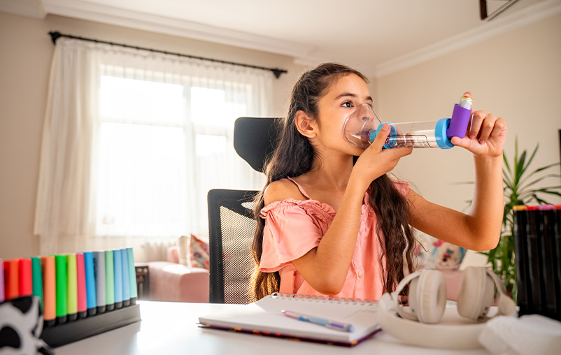 A girl uses an inhaler with a spacer