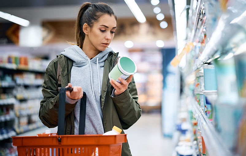 A woman at a grocery store looking over a product food label that she is interested in purchasing.