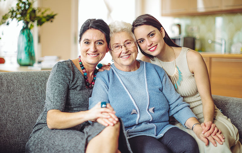 Three generations of women from a family sitting on a couch in their home.