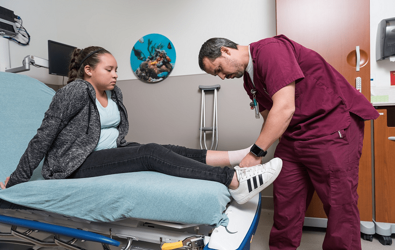 Physician in the University Health pediatric emergency department bandaging patient’s ankle.