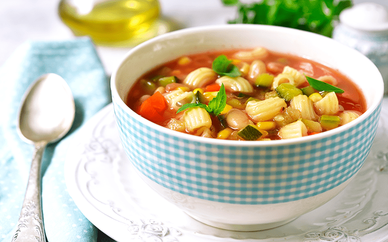 Minestrone soup in a bowl on a light slate, stone or concrete background.