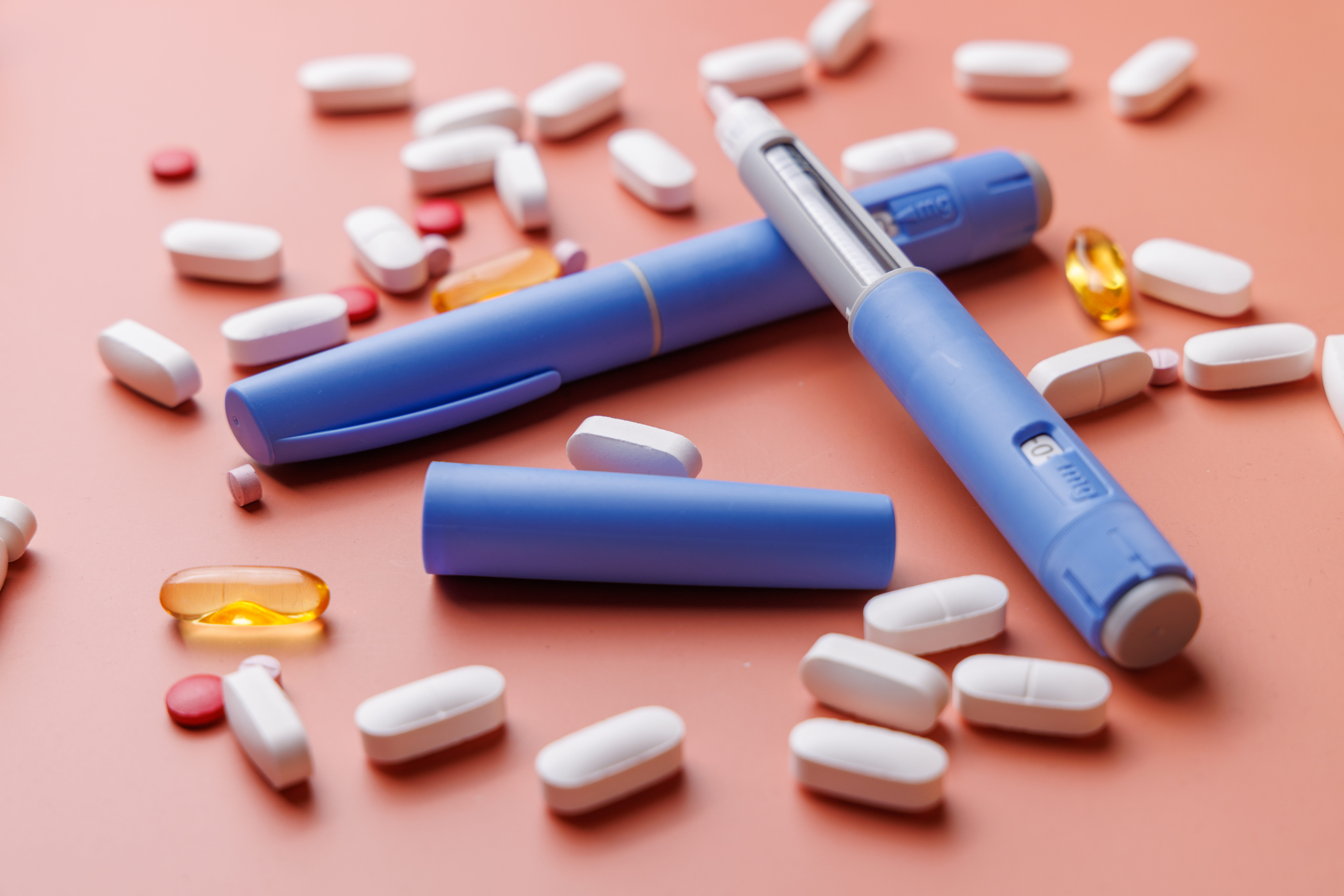 Semaglutide injection pens with mixed colorful pills on cream background.