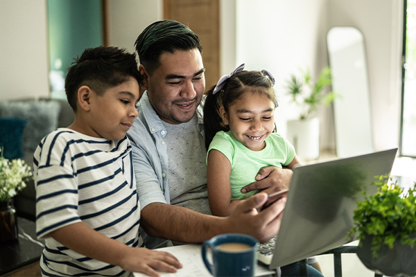 A father and two children look at a laptop.
